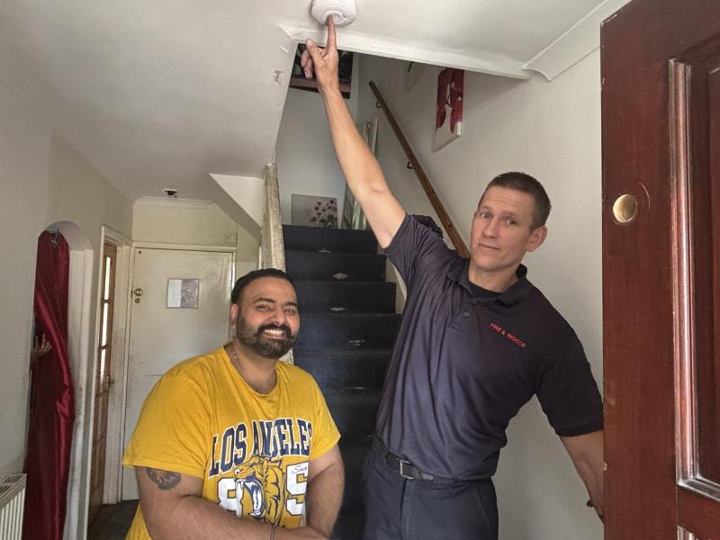 A firefighter and Jatinder pose for a photograph with the newly installed smoke alarm.