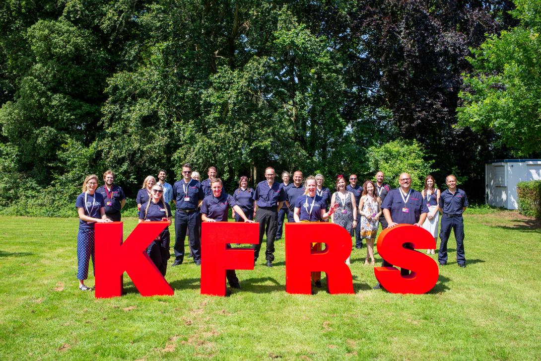 A mixed group of Kent Fire and Rescue Service colleagues standing behind giant red letters spelling KFRS