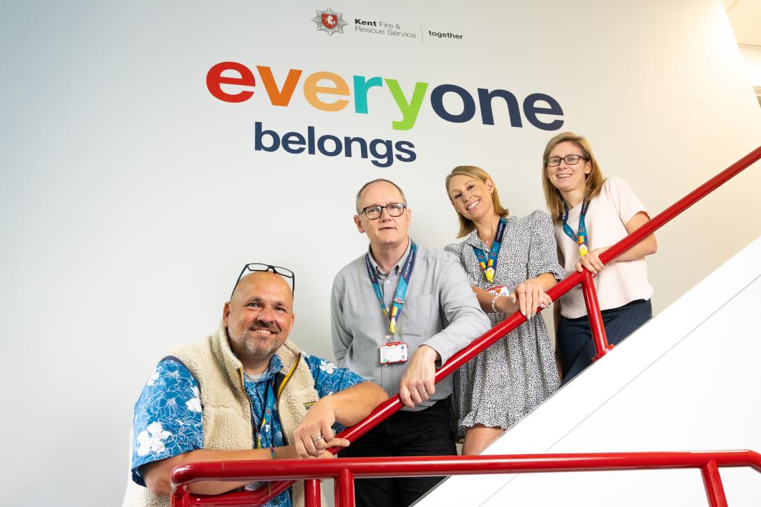 colleagues standing on stairs smiling at the camera with 'everyone belongs' written on the wall behind them