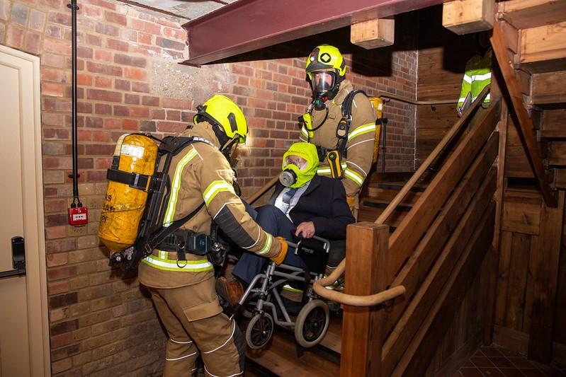 firefighters carrying main in wheelchair downstairs