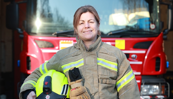 Photo of a firefighter standing in front of a fire engine wearing protective uniform