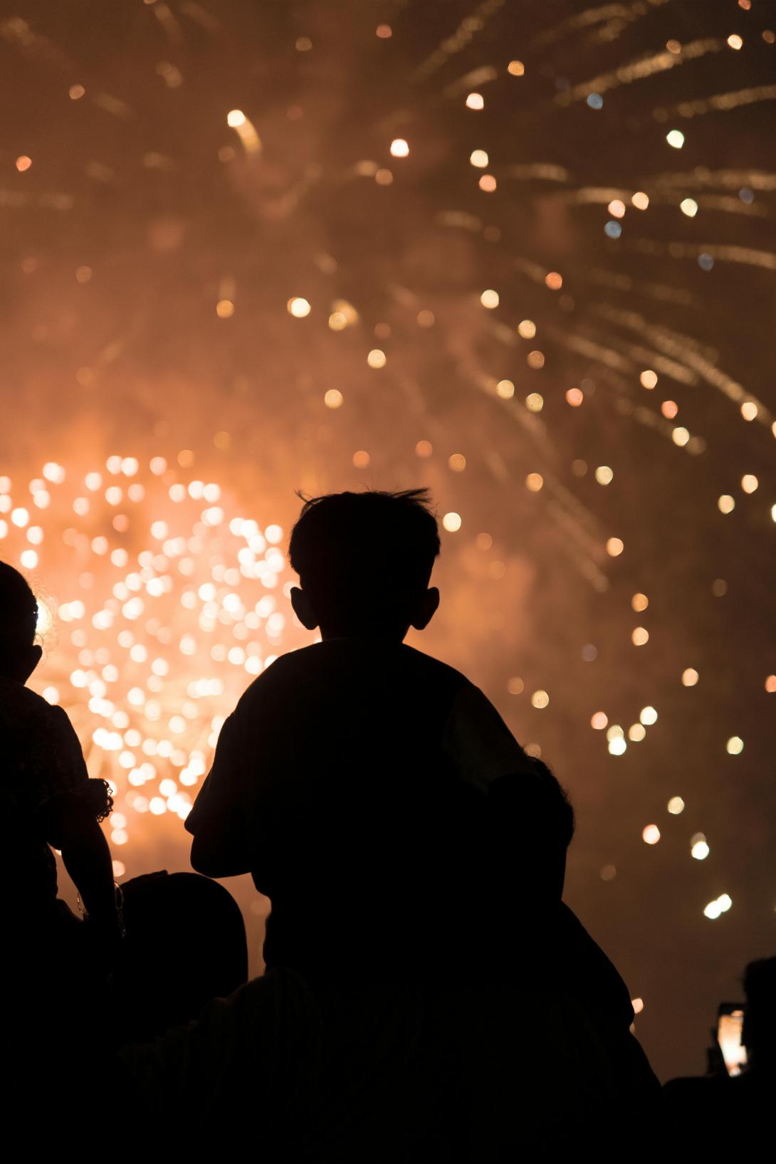 Silhouette of child on an adults shoulders watching fireworks