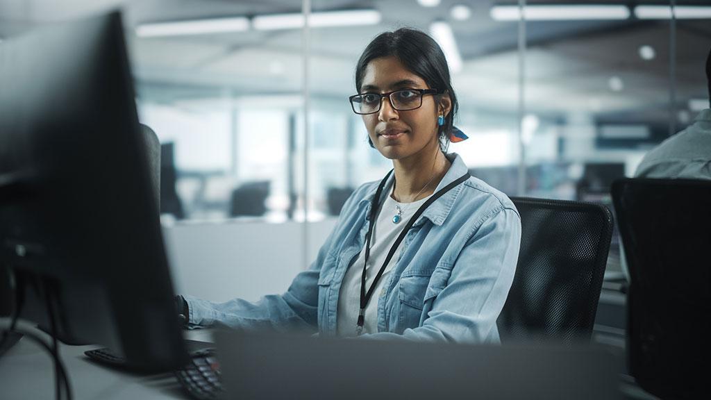 A woman wearing glasses works at a computer in an office